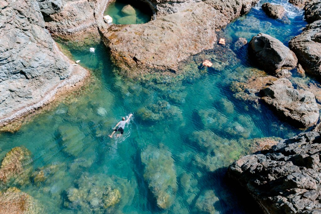 A captivating aerial shot of a swimmer in a turquoise tidal pool surrounded by rocky formations.