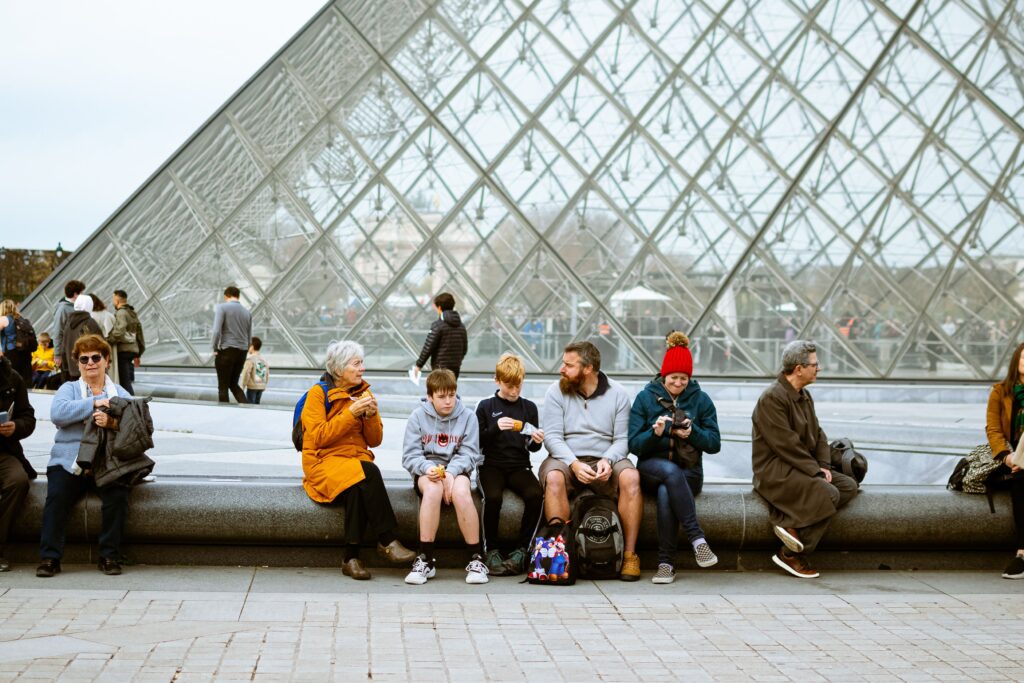 A diverse group of people sitting near the iconic Louvre Pyramid in Paris, enjoying a casual day outdoors.